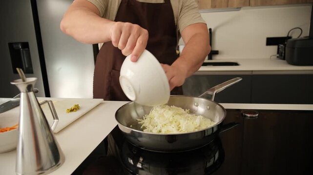 Male cook adding chopped cabbage, onions, and carrots into a frying pan on an induction stove