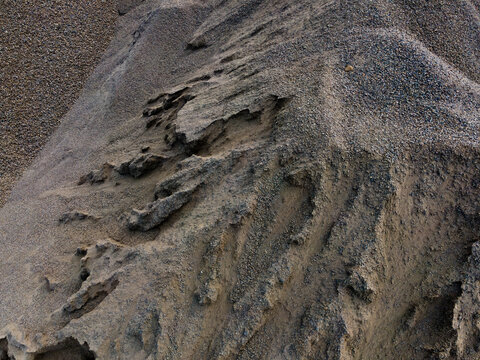 Aerial Top-Down View of a Large Aggregate Stockpile with Distinctive Dune-Like Surface Textures at a Mining Site. Industrial Landscape and Abstract Geological Texture Viewed from Above.