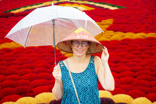 A woman in a conical hat with an umbrella among multi-colored incense sticks. Quang Phu Cau, Hanoi, Vietnam.