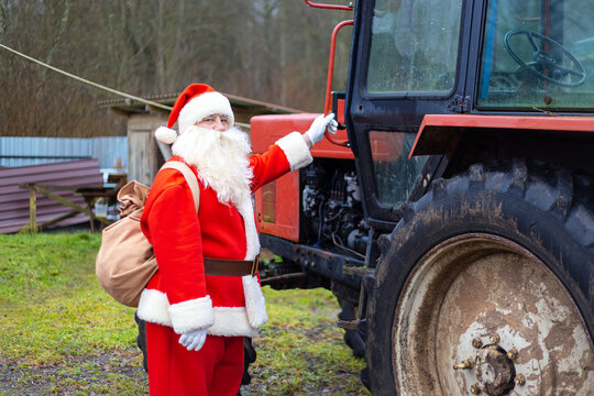 Authentic Santa Claus next to a red tractor. Delivering gifts to hard-to-reach areas.