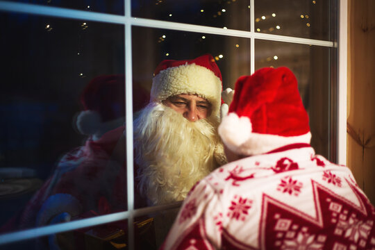 Cute boy in a Santa hat looking out the window. An authentic Santa Claus stands outside.
