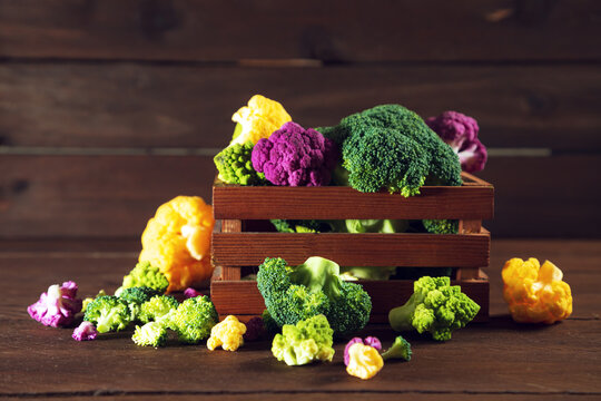 Colorful cauliflower in a wooden crate on a table. Purple, yellow, and green florets.