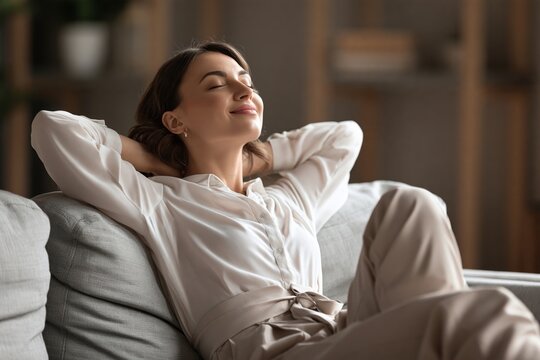 Relaxed young woman leaning back on a comfortable couch with eyes closed and smiling softly