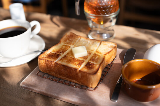 Thick buttered toast and coffee on a wooden table in morning light