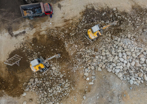 Yellow Excavators and a Heavy Truck Working Near Large Piles of Boulders and Rocks in a Rock and Sand Quarry in Indonesia. Mining Site and Heavy Machinery Viewed from Above.