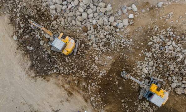 Yellow Excavators and a Heavy Truck Working Near Large Piles of Boulders and Rocks in a Rock and Sand Quarry in Indonesia. Mining Site and Heavy Machinery Viewed from Above.