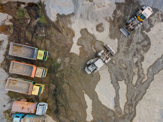 Aerial Scenery of Wheel Loader and Several Haul Trucks Working in a Rock and Sand Quarry with Distinctive Ground Patterns, Industrial Mining Site view from above. © katakaneh