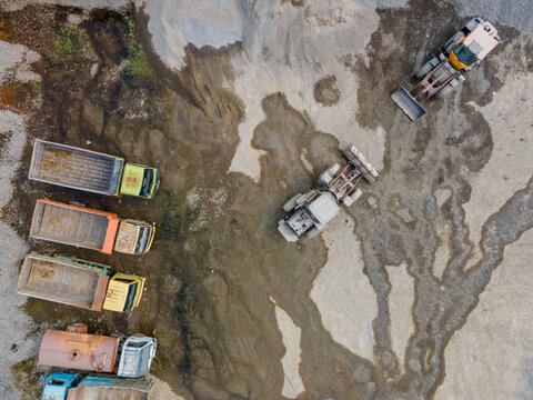 Aerial Scenery of Wheel Loader and Several Haul Trucks Working in a Rock and Sand Quarry with Distinctive Ground Patterns, Industrial Mining Site view from above.