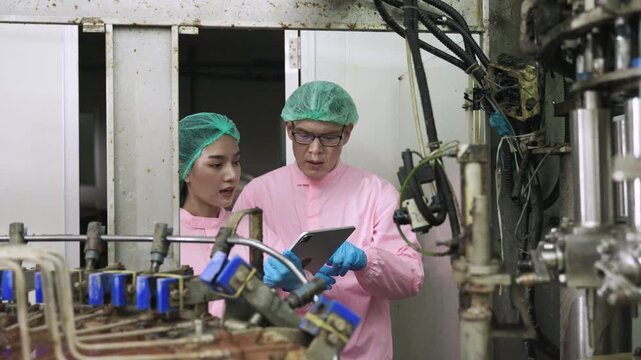 Professional Asian maintenance engineer and technician in food and beverage drink factory in uniform with tablet while talking and discussing machine operation in production line at industry facility.