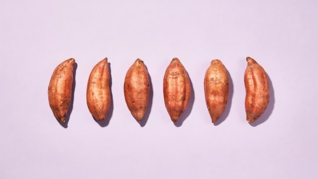 Six organic raw sweet potatoes in a row on a pastel violet background
