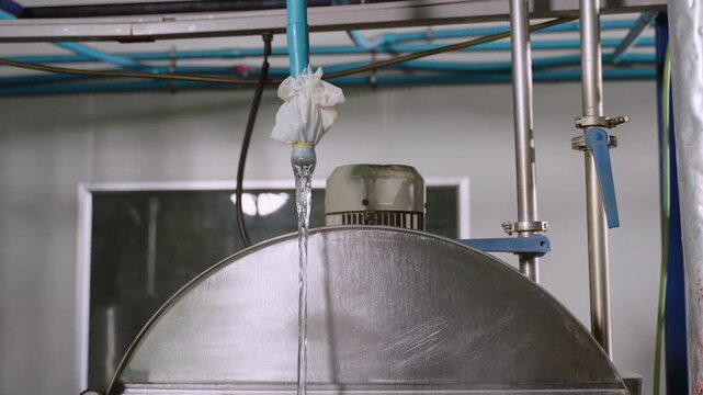 Pure water flowing from the pipe into the beverage mixing liquid boiler tank while smoke and steam rise from the boiler into air in factory production line in food and drink manufacturing industry. 