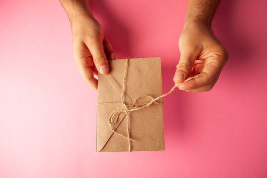 Gift box wrapped in craft paper and tied with twine on pink background