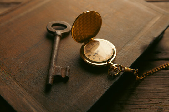 Vintage pocket watch, key and old book on wooden background.