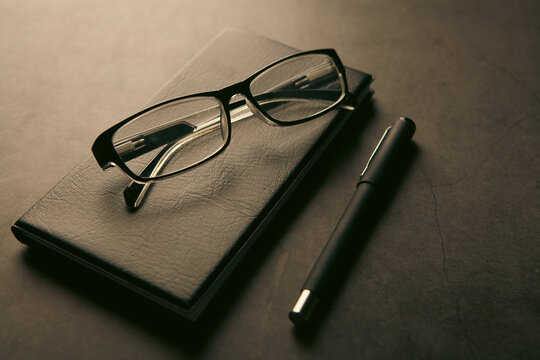 Notebook with pen and eyeglasses on black stone background.