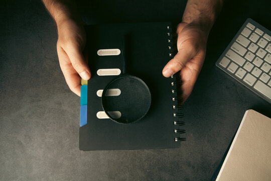 Man looking through a magnifying glass at a notebook on a dark background