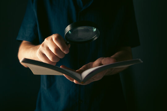 Man looking through a magnifying glass at a notebook on a dark background