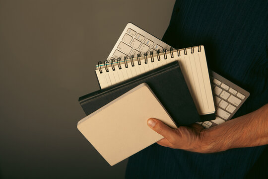 Businessman holding folders and computer keyboard on dark background, closeup