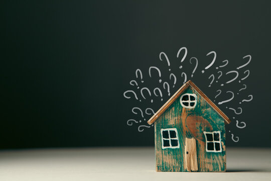 Conceptual image of question mark with wooden house on dark background
