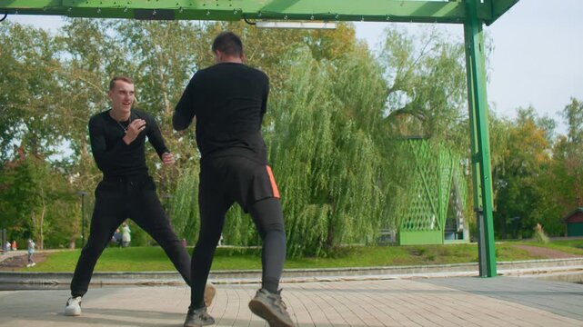 two men practicing close quarters defense under metal pergola in urban park executing clinch and counter drills grip control and momentum shifts tactical focus realistic scenario training intense