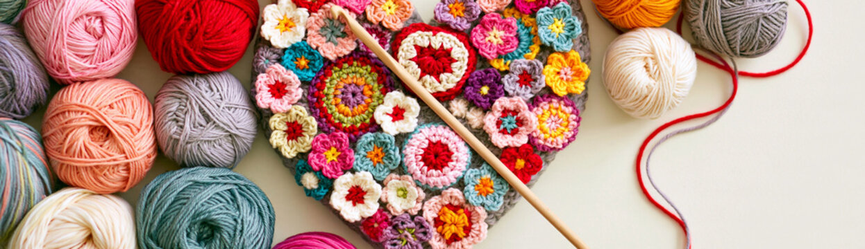 Heart shape made of colorful crochet flowers and yarn skeins with knitting needle, a crafting concept for handmade gifts and hobbies, showcasing textile art and creative expression with wool