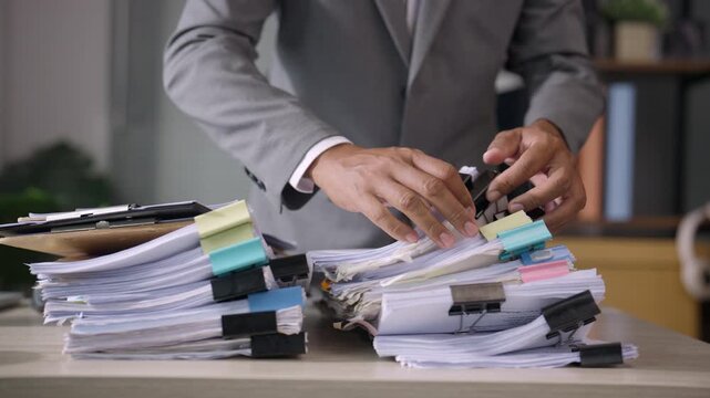 Businessman Organizing Large Stacks of Paper Documents at Office Desk