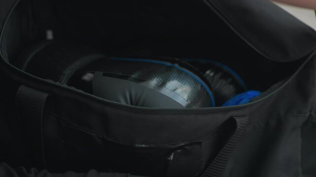 hand reaching into black bag pocket, revealing bright blue hand wrap and padded glove, careful retrieval, tattooed arm in motion, intimate closeup of interior compartment, early morning practice vibe