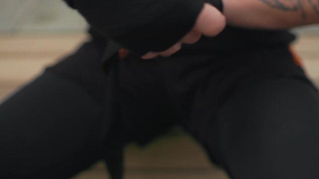 caucasian boxer wrapping hands in gym with black wraps and visible tattoos, closeup of fingers and wrists as athlete methodically secures tape, focused preparation and intensity before training