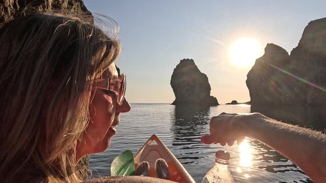 Traveler drinking water inside sea cave during sunset. Static close-up shot captures backlighting reflecting on the ocean surface and plastic bottle.