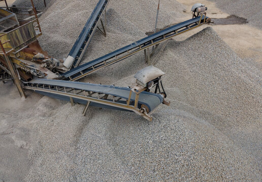 Multiple Conveyor Belt Systems and Large Aggregate Stockpiles at an Industrial Quarry Facility. Rock Processing and Bulk Aggregate Transportation, Industrial Mining Site view from above.