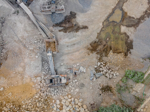 Rock Crusher Machinery Near Large Boulders and Split Rocks and Wet Ground Areas at an Industrial Quarry Site, Industrial Mining Site view from above.
