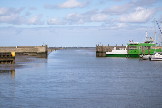  Scenic view of the harbor entrance in Neuharlingersiel with green island ferry at low tide under a blue sky, East Frisia, Germany.
