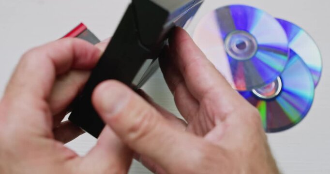 In a close-up, a person examines a large video VHS cassette, opens the flap, and reveals its wide magnetic tape.