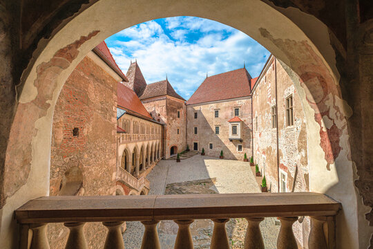 Corvin Castle's historic courtyard with Renaissance and Gothic architecture of Transylvania, viewed through an arched stone balcony, presenting medieval charm under a vibrant sky in Hunedoara, Romania