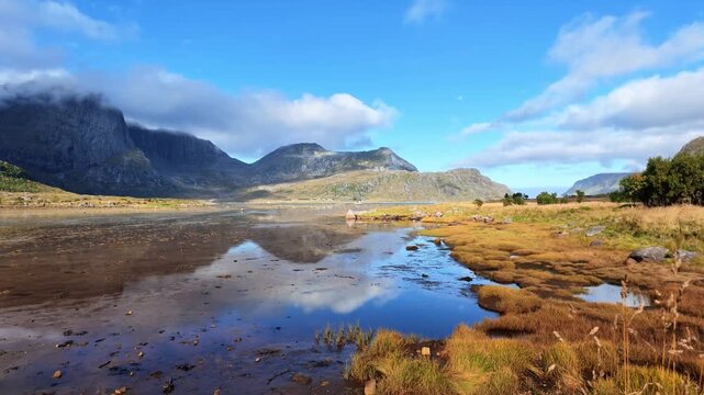 View near Flakstadpollen with water, reflections, green mountains and low clouds in the impressive Lofoten landscape.