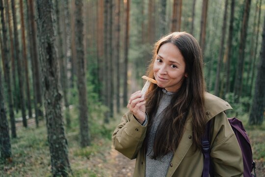 Smiling woman holding a freshly picked wild mushroom in a pine forest, enjoying seasonal foraging, mushroom hunting, hiking and peaceful outdoor recreation.