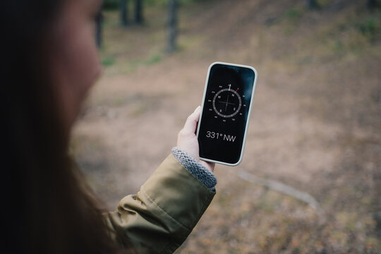 Woman using a smartphone compass while navigating through a forest trail, illustrating outdoor orientation, hiking technology, direction finding and nature exploration.
