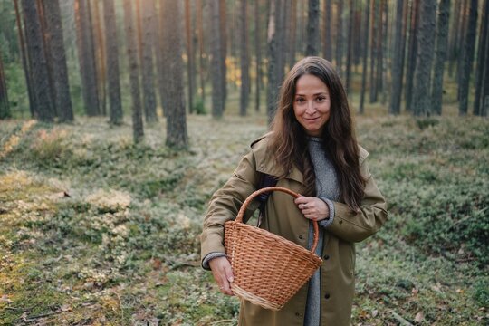 Woman standing in a pine forest with an empty wicker basket, ready for seasonal mushroom and berry foraging, nature exploration and peaceful outdoor recreation.