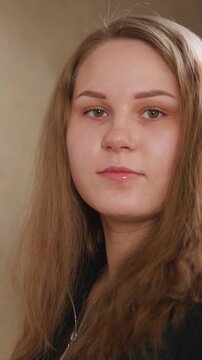 Close up side profile shot shows woman with long brown hair in black zip up jacket. soft lighting highlights her features and texture of her clothing against plain neutral background