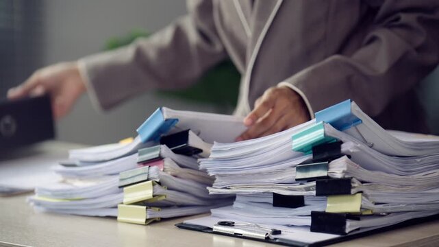 Office Worker Organizing Large Stacks of Paper Documents at Desk