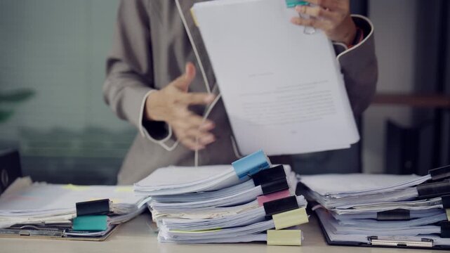 Office Worker Reviewing Large Stack of Paper Documents at Busy Desk