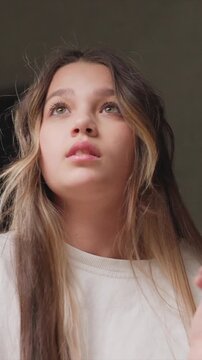 Close up view of young woman with long hair wearing white top focusing on her upper body and hands as woman interacts with orange object. background is dark or neutral emphasizing subject