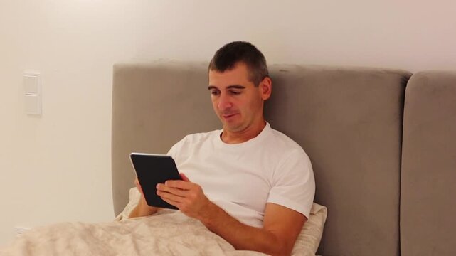 Man Relaxing in Bed and Reading an E-Book in the Evening