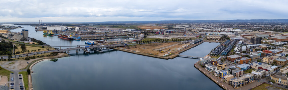 Panoramic aerial drone view overlooking the Port Adelaide River, South Australia's historic port precinct, Tom 'Diver' Derrick Bridge, cargo shipping docks, and industrial facilities. Economy concept.