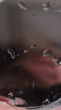 Water droplets cling to edge and smooth surfaces. background is blurred with soft lighting creating reflections and highlights on shiny textures. hand occasionally appears suggesting