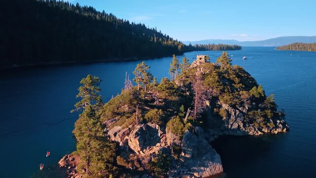 Fannette Island and its summit teahouse in Emerald Bay. Conifers cover a rocky island below stone ruins, with dark blue water and a shaded hillside behind.