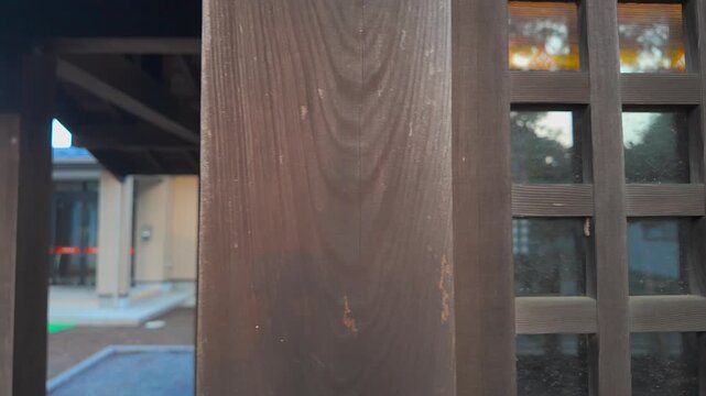Close-up of a traditional Japanese wooden lattice window with glass reflecting historic architecture in Japan. The camera smoothly slides left past the dark wood frame, evoking calm and Zen.