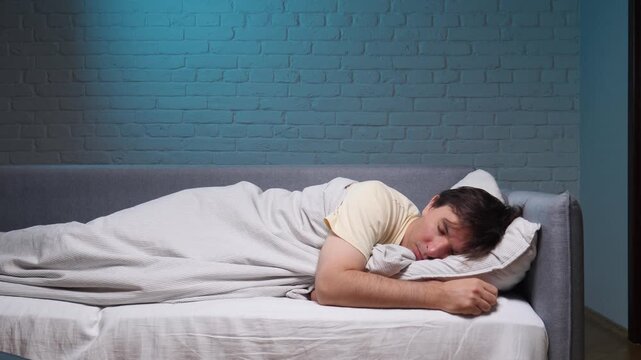 Man resting comfortably on a bed at night, sleeping peacefully under a duvet against a warm brick wall, enjoying quiet relaxation and restorative deep sleep in a cozy home setting