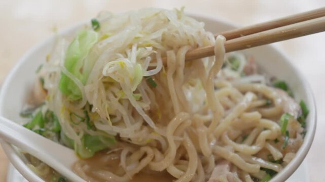 Chopsticks lifting thick noodles from Jiro style ramen