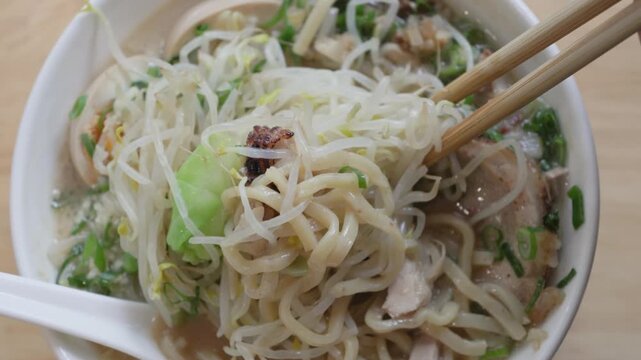 Chopsticks lifting noodles and bean sprouts from ramen