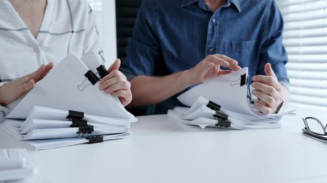 Colleagues reviewing financial data, examining documents, and organizing files with binder clips in an office, managing business paperwork and accounting workload